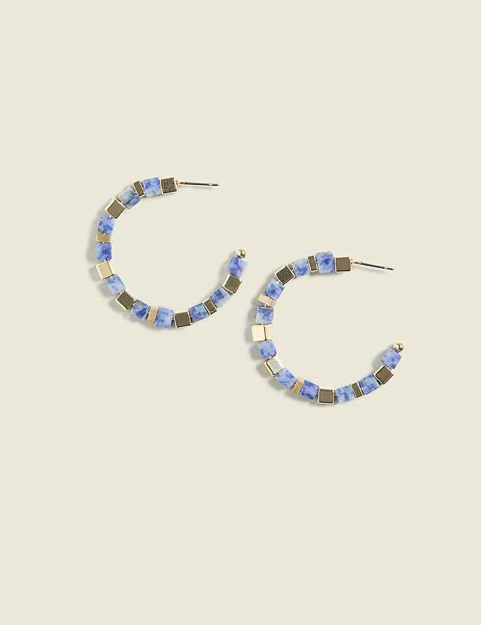 A pair of blue and gold beaded hoop earrings rests on a pale green background.