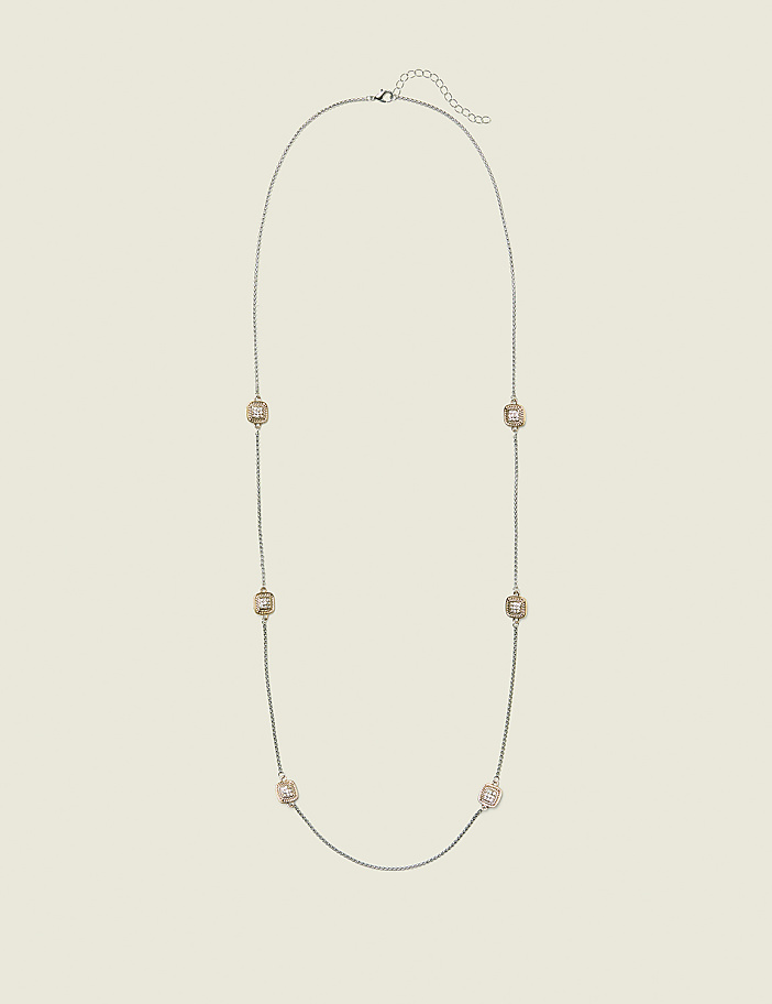 A long, delicate silver chain necklace with seven square, rose-gold toned charms is laid out against a plain, light beige background.