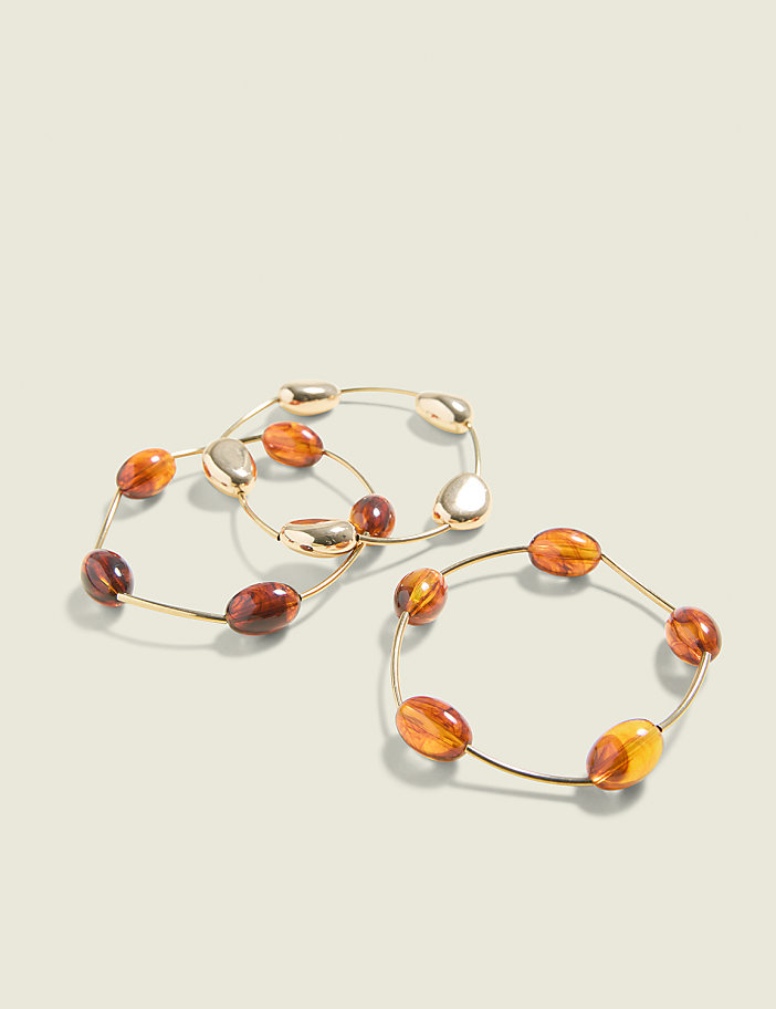 Three gold bangles with amber-colored beads are arranged on a light beige background.