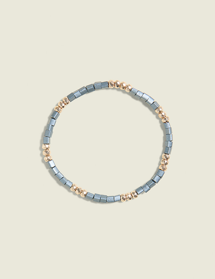 A bracelet of gray and gold beads is centered on a pale yellow background.