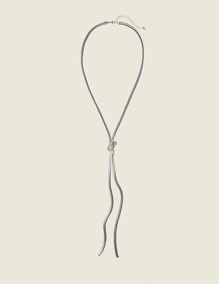 A silver knot necklace with dangling chains rests against a plain, light beige background.