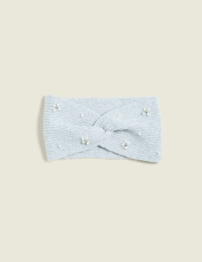 A light blue, fuzzy headband with a twisted knot and scattered pearl and rhinestone embellishments rests on a pale blue background.