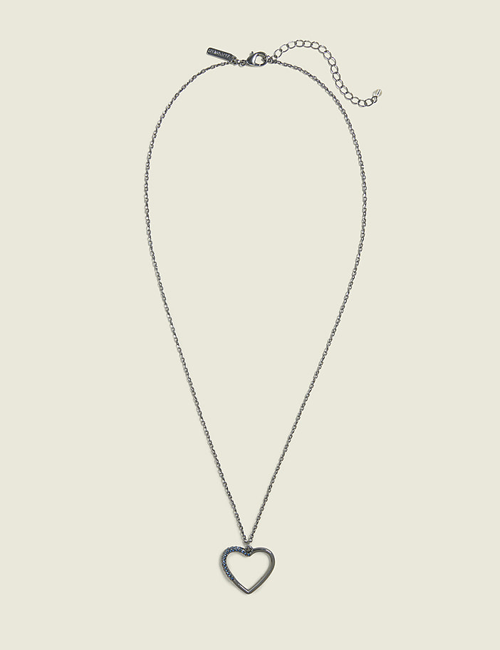 A silver heart pendant hangs from a delicate chain against a plain, light beige background.