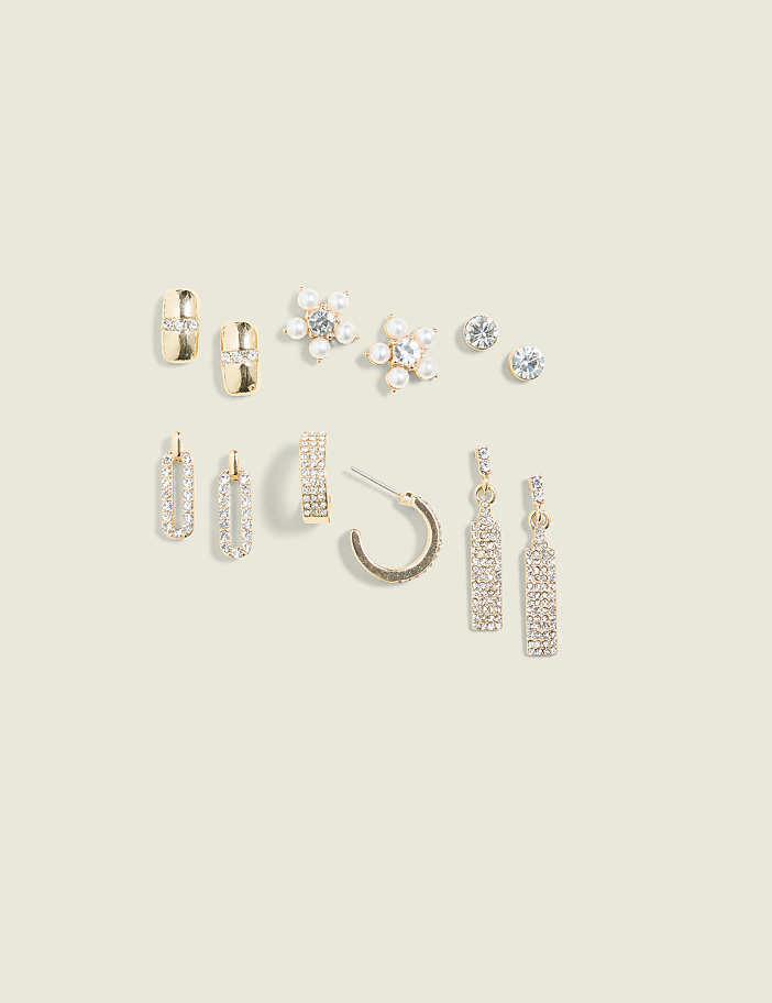 A collection of gold and silver earrings, some with rhinestones and pearls, are arranged on a pale yellow background.
