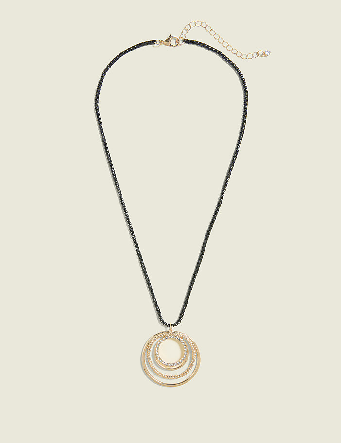 A gold pendant with three nested, sparkling rings hangs from a dark chain against a plain, light beige background.