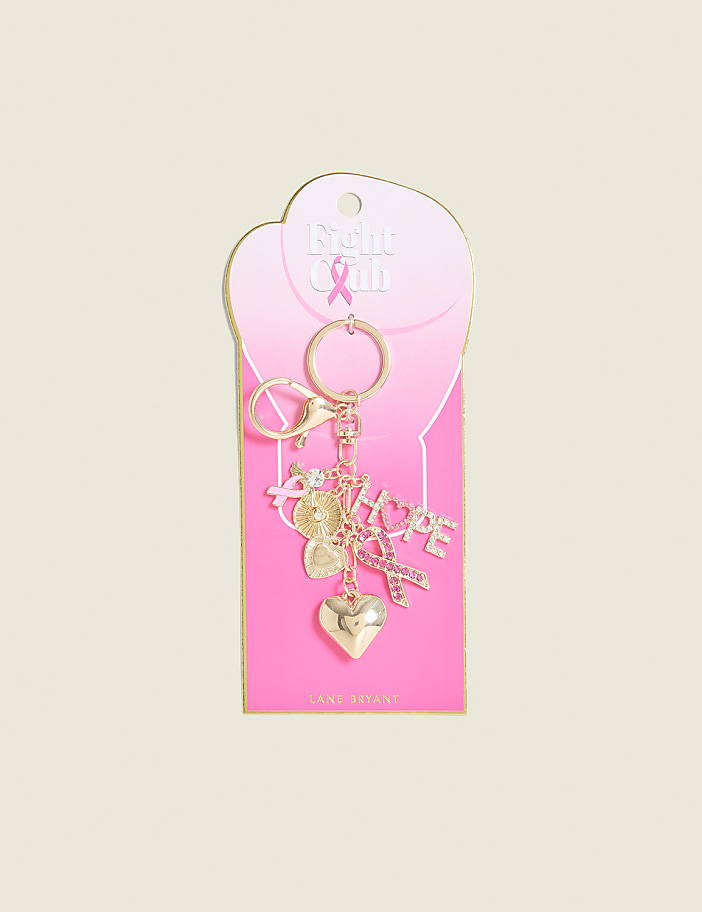A gold keychain with various charms, including a heart and the word "hope," hangs from a pink card with a breast cancer awareness ribbon, set against a pale pink background.
