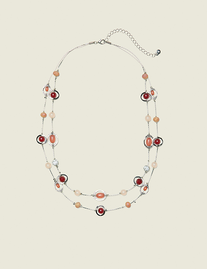 A delicate, multi-strand necklace with coral and clear beads is displayed against a plain, light beige background.