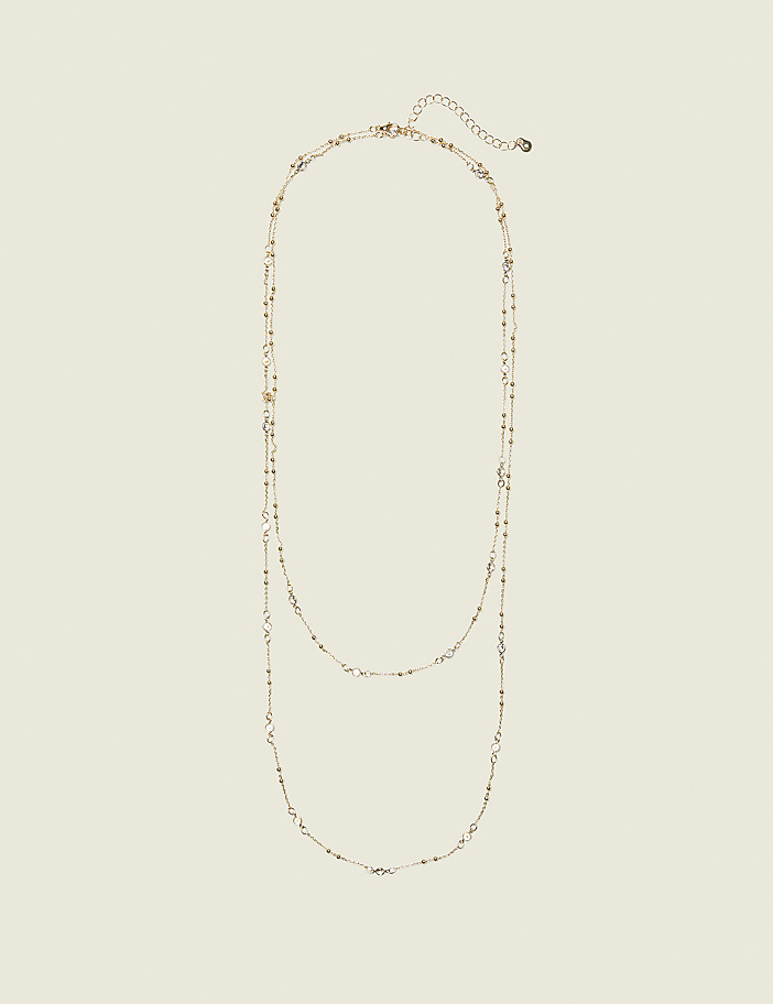 A delicate gold necklace with small charms is laid out against a plain, light beige background.