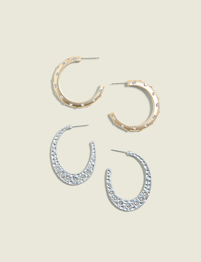 Two pairs of hoop earrings, one gold and one silver, are arranged on a pale yellow background.