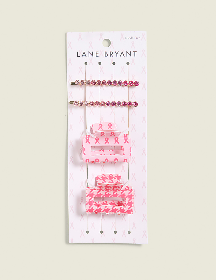 Four pink hair accessories, including two jeweled bobby pins and two patterned claw clips, are displayed on a white card with a pink ribbon pattern against a light beige background.