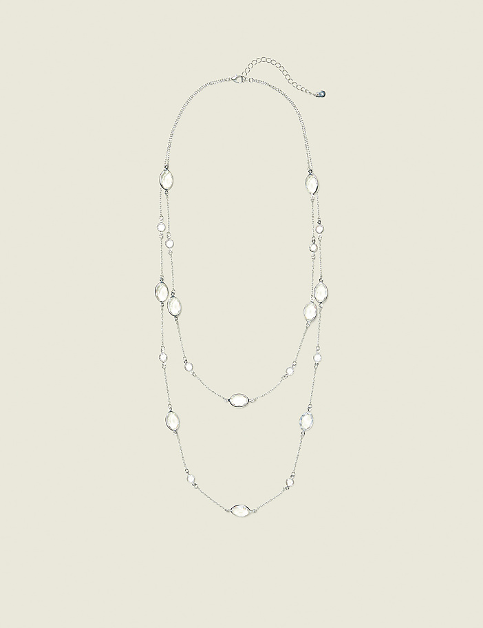 A delicate silver necklace with clear oval-shaped pendants is displayed against a plain, light beige background.