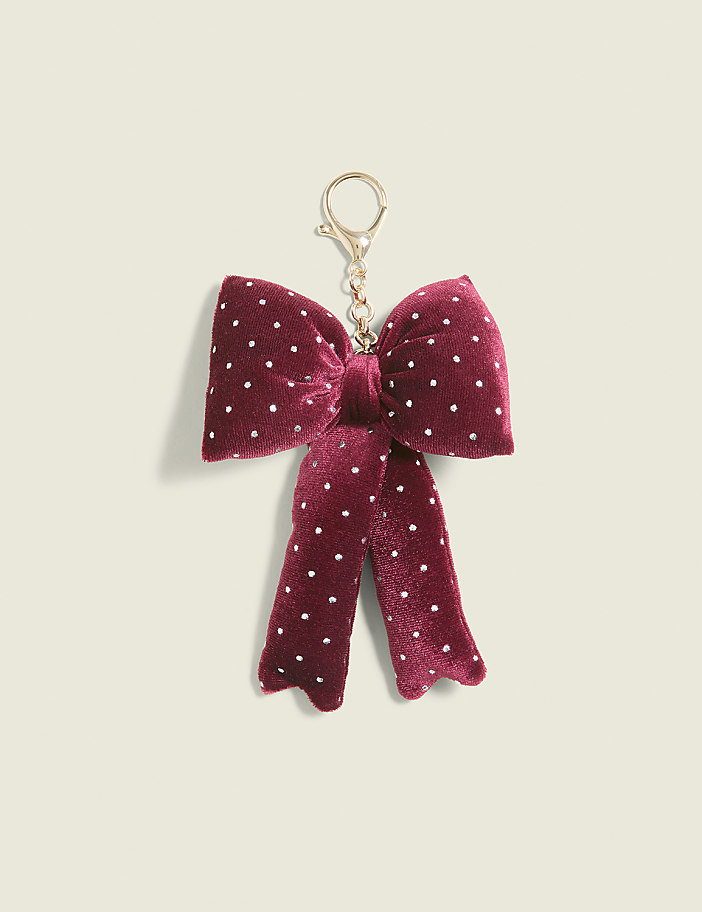 A burgundy velvet bow keychain with white polka dots hangs against a plain, light beige background.