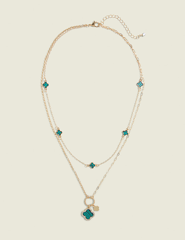 A delicate gold necklace with teal clover charms hangs against a plain, light background.