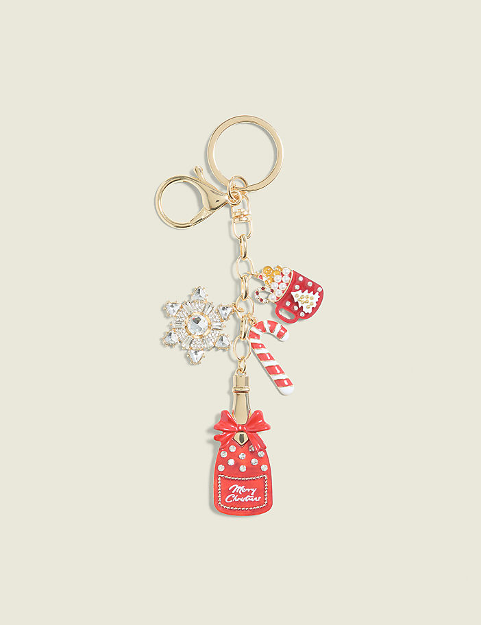 A festive Christmas-themed keychain with a red bottle, candy cane, snowflake, and hot chocolate charm hangs against a plain cream background.