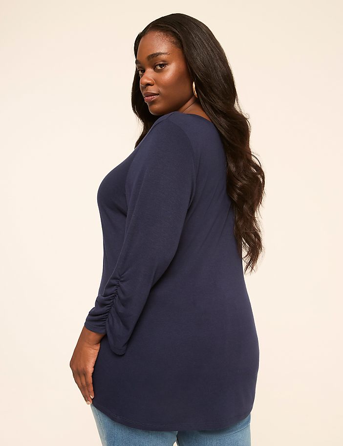 A woman in a navy blue top stands against a plain, light-colored background.
