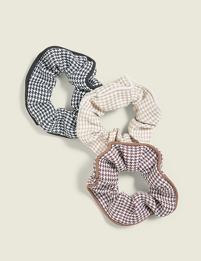 Three houndstooth scrunchies with contrasting trim are arranged on a pale yellow background.