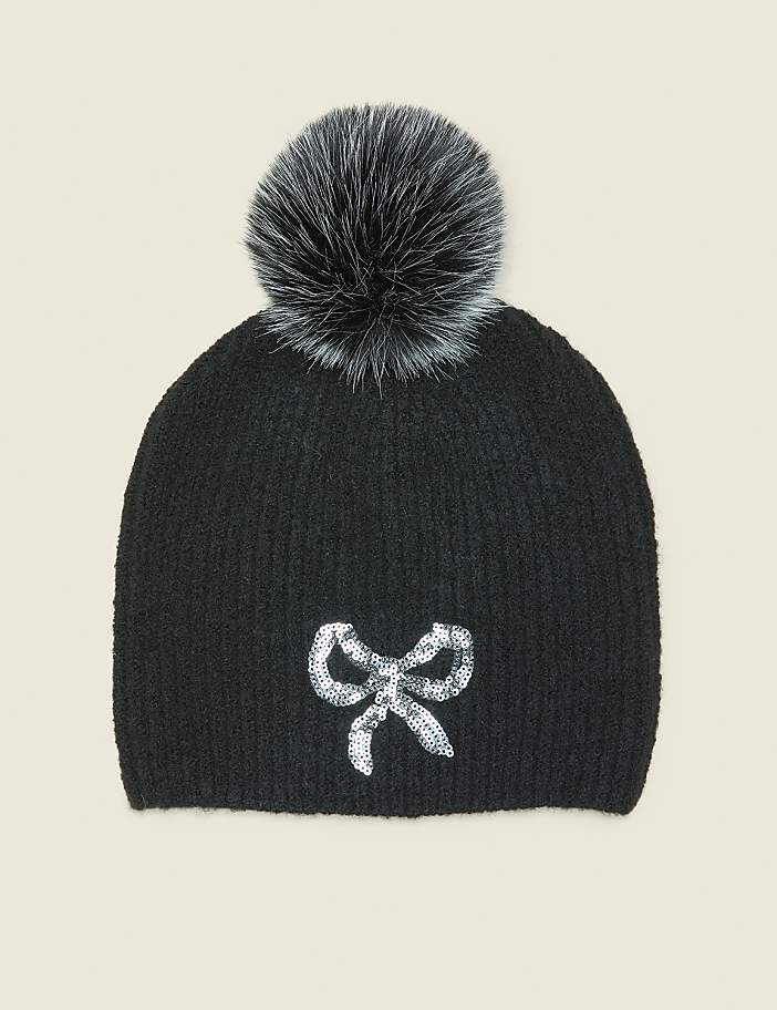 A black knit beanie with a sparkly bow applique sits against a plain, light-colored background.