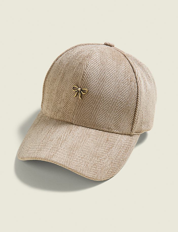 A beige herringbone baseball cap with a small gold bow accent sits on a plain, light beige background.