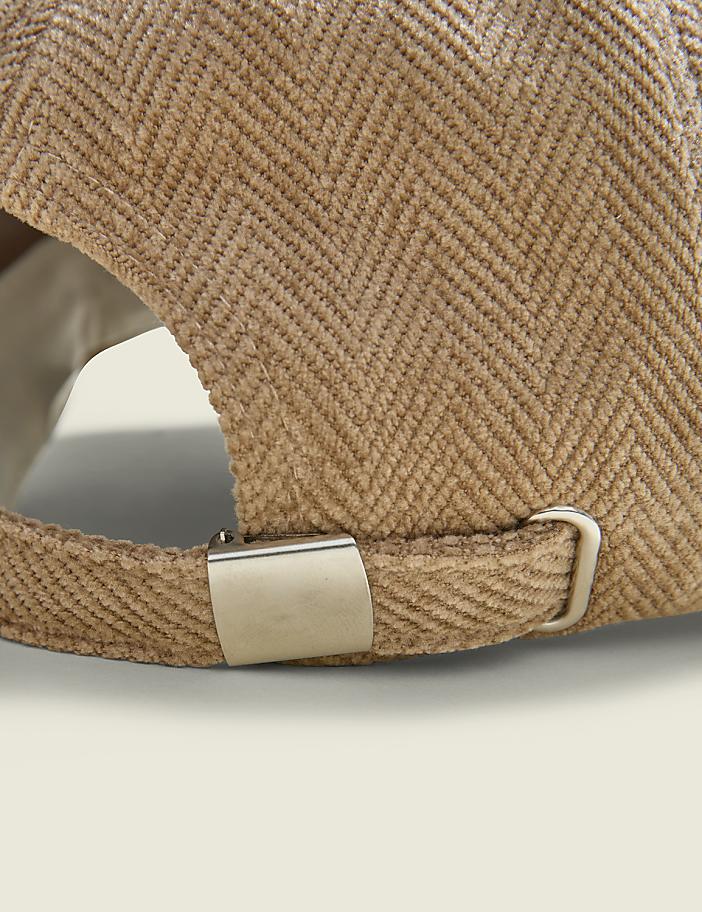 A close-up of the back of a tan herringbone baseball cap with a metal buckle is shown against a plain, light-colored background.