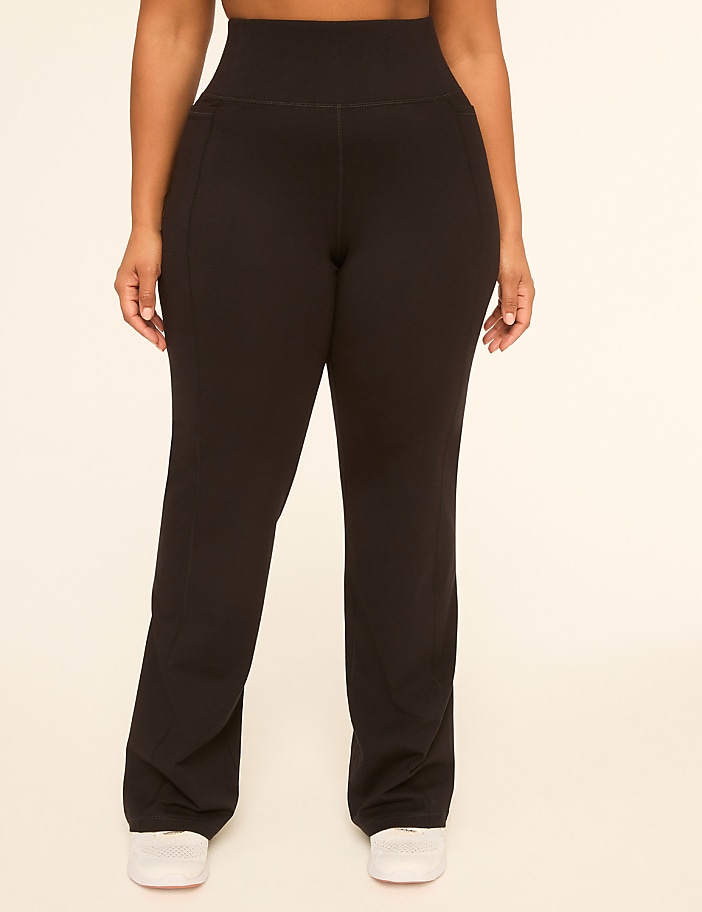 A person stands in black flared yoga pants and white sneakers against a plain, light-colored background.