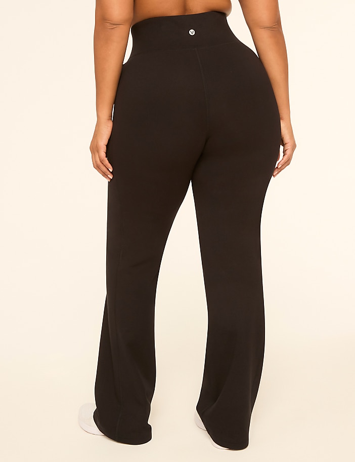 A person wearing black flared yoga pants stands against a plain, light-colored background.