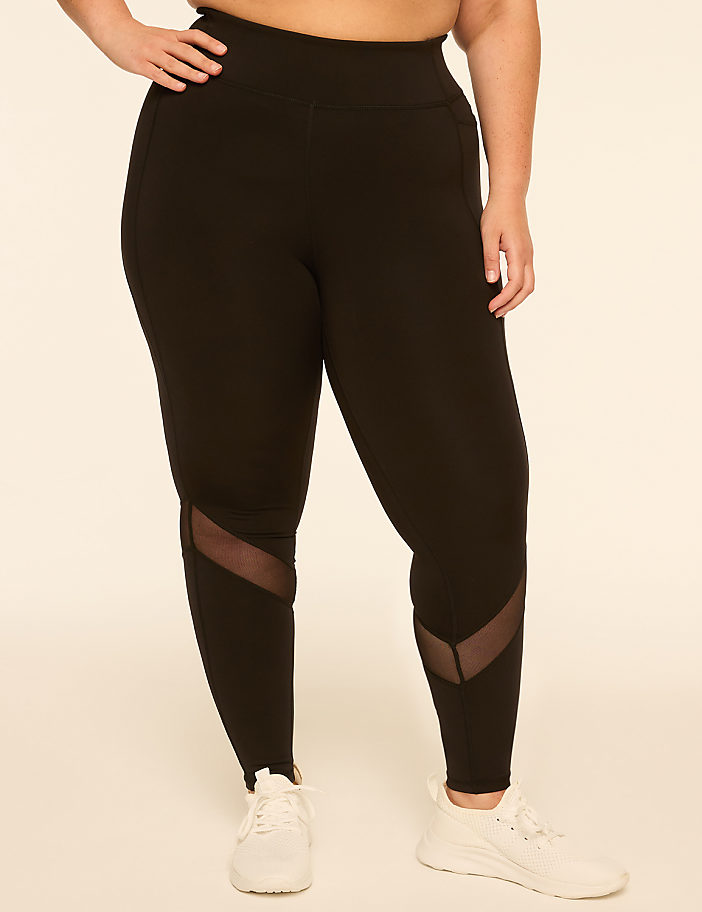 A person wearing black leggings with mesh accents on the lower legs stands against a plain, light-colored background.