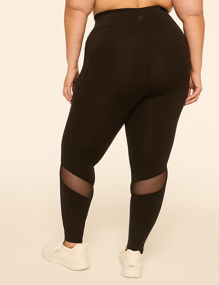 A person wearing black leggings with mesh inserts on the calves stands against a plain, light-colored background.