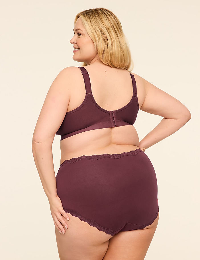 A woman in a plum-colored bra and high-waisted briefs stands against a plain, light-colored background.