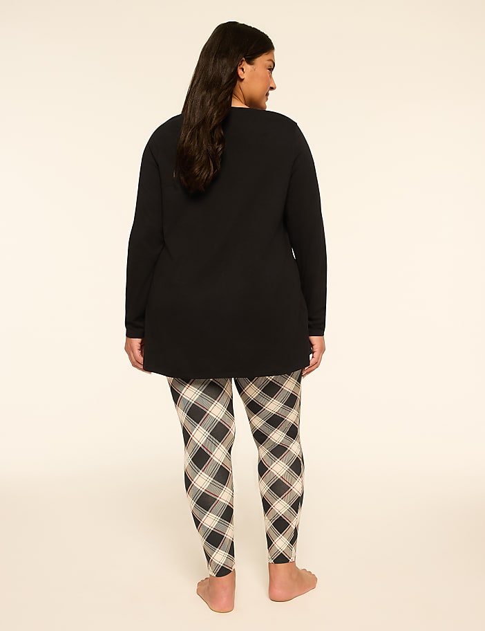 A woman in a black top and plaid leggings stands against a plain, light-colored background.