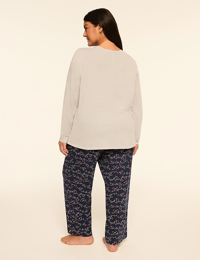 A woman stands facing away from the camera in a light gray long-sleeved shirt and navy blue patterned pajama pants against a plain, light-colored background.
