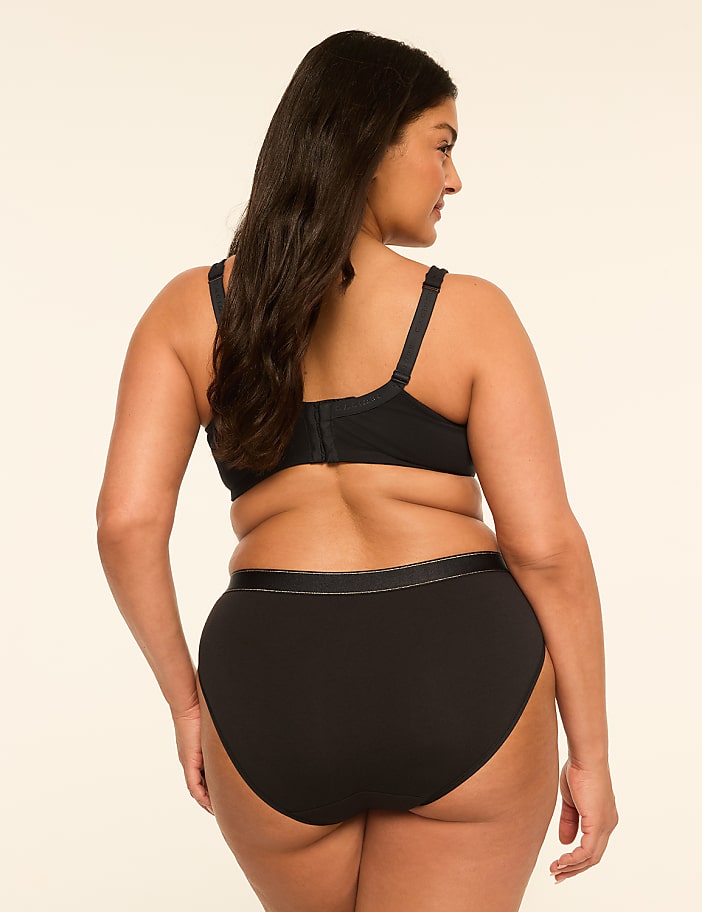A woman in black lingerie stands against a plain, light-colored background.