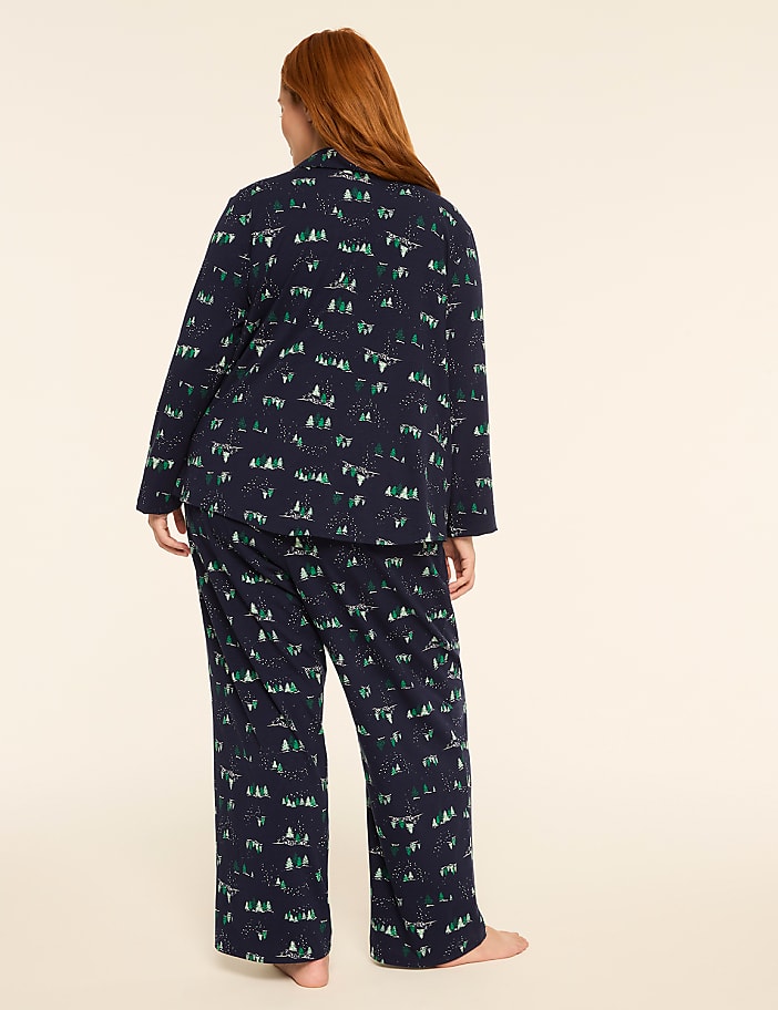 A woman in navy blue pajamas with a forest and animal print stands against a plain, light-colored background.