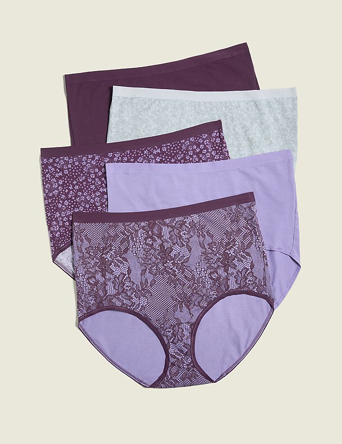 A stack of five pairs of women's underwear in various shades of purple and grey, with floral and lace patterns, are arranged on a plain, light brown background.