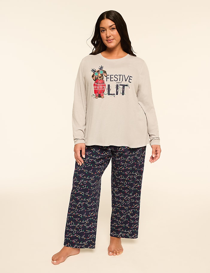 A woman stands in festive pajamas with a graphic on her shirt, against a plain, light-colored background.