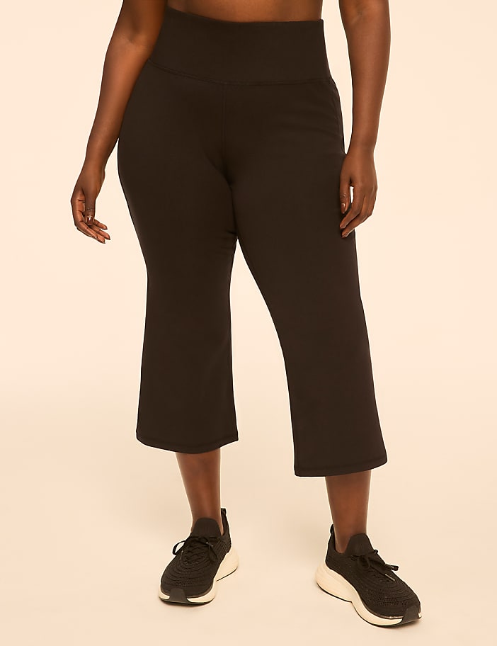 A person wearing black capri leggings and athletic shoes stands against a plain, light-colored background.
