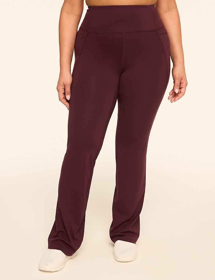 A person wearing maroon flared yoga pants stands against a plain, light-colored background.