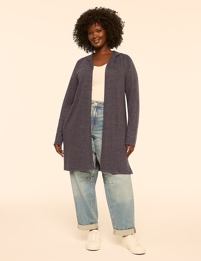 A woman in a blue cardigan stands against a plain, light-colored background.