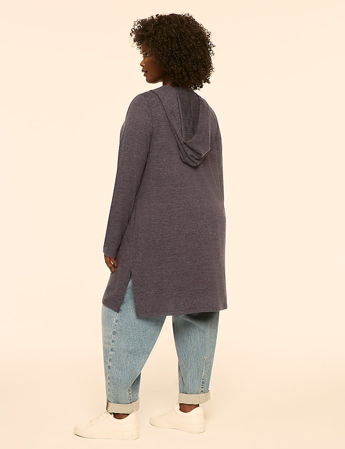 A woman in a blue hooded cardigan stands against a plain, light-colored background.