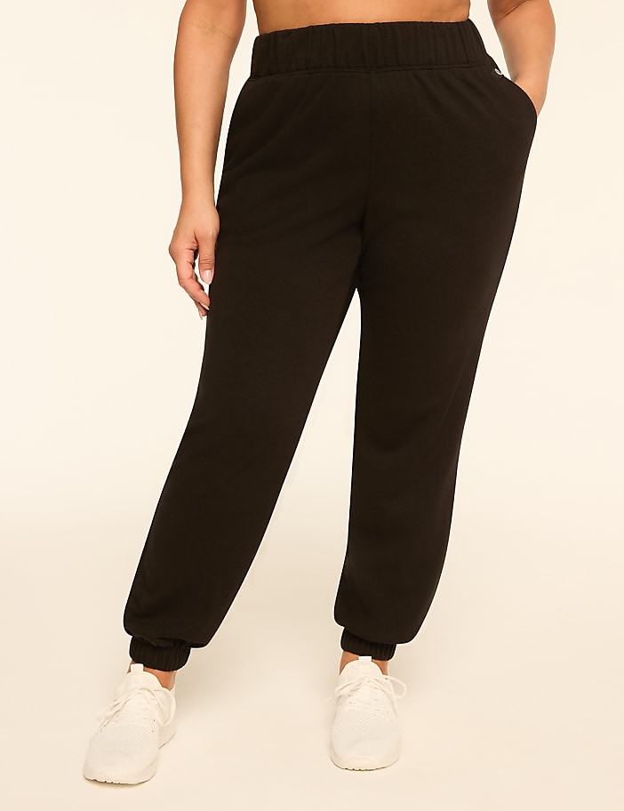 Black sweatpants with white sneakers are worn by a person against a plain, light-colored background.
