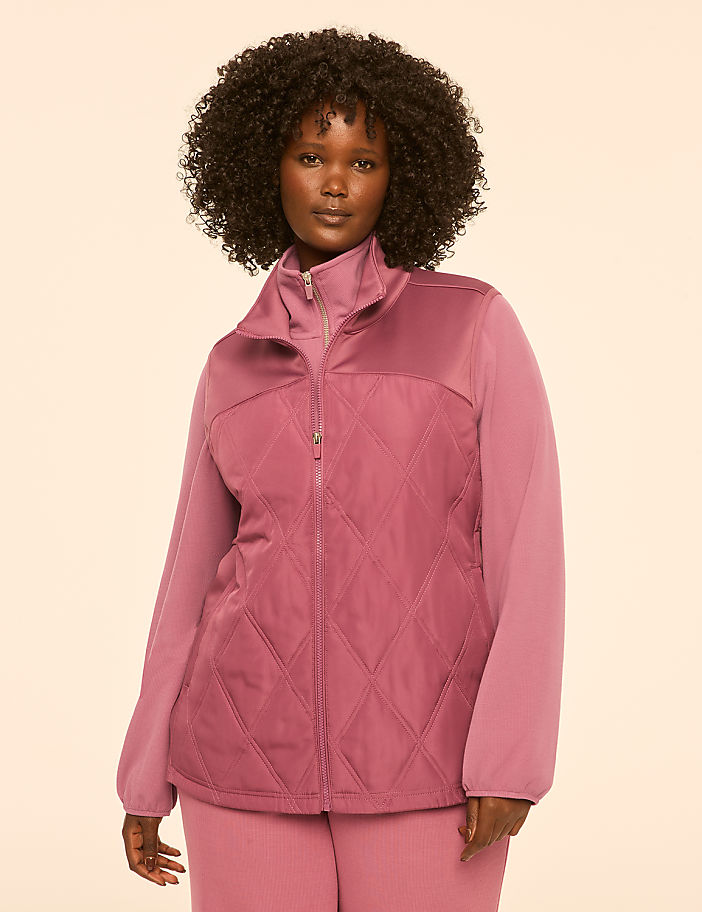 A woman in a pink quilted jacket and pants stands against a plain, light-colored background.