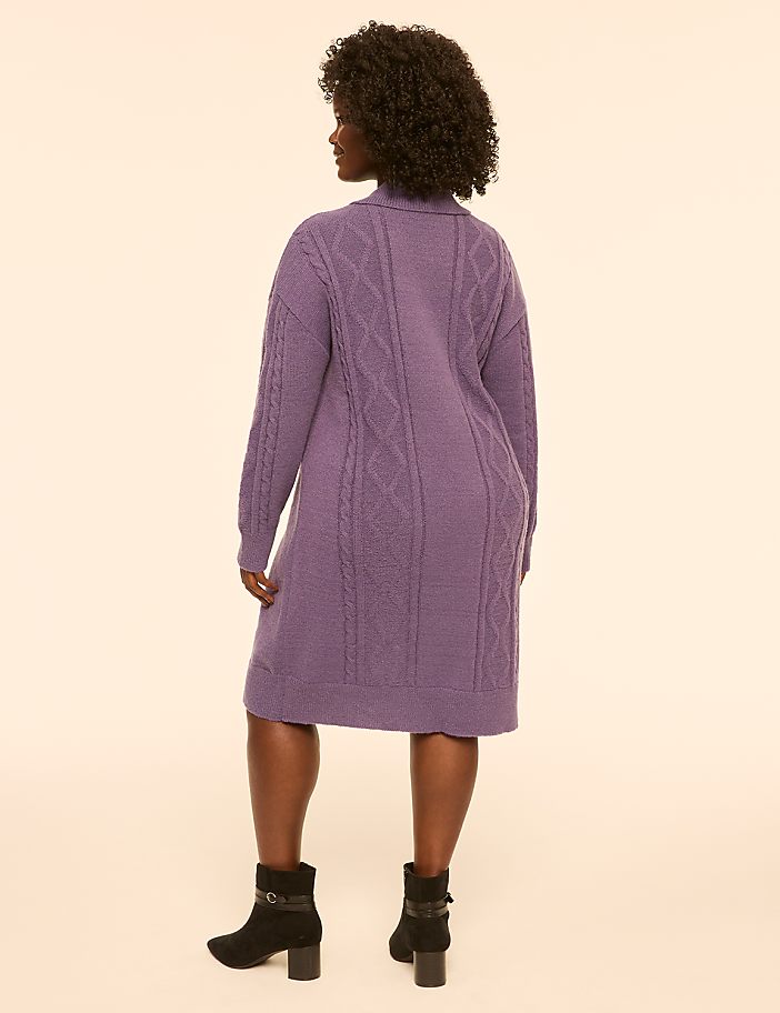 A woman in a purple cable-knit dress and black boots stands against a plain, light-colored background.