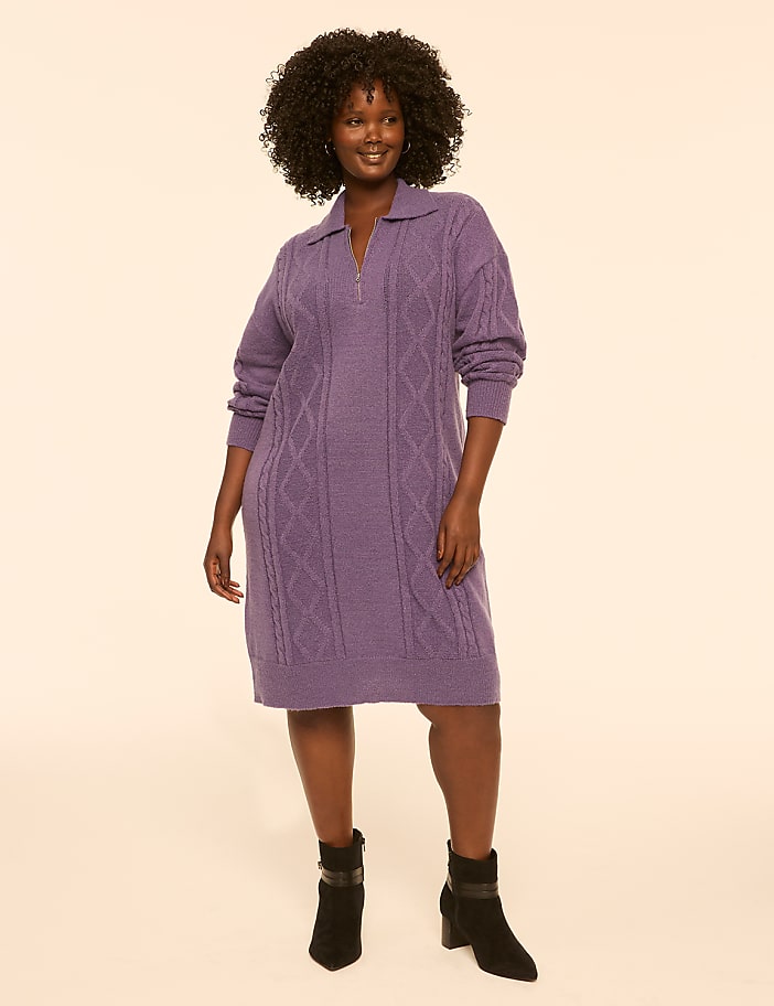A woman in a purple cable-knit dress and black boots stands against a plain, light-colored background.