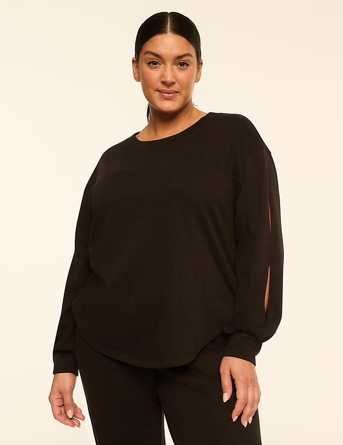 A woman in a black top with cutouts on the sleeves stands against a plain, light-colored background.