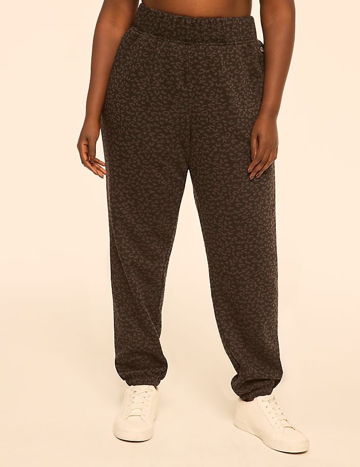 A person wearing leopard-print sweatpants and white sneakers stands against a plain, peachy-toned background.