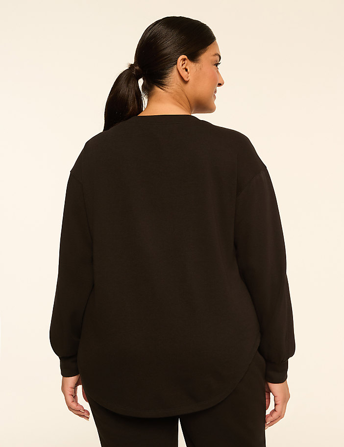 A woman in a black sweatshirt stands against a plain, light-colored background.