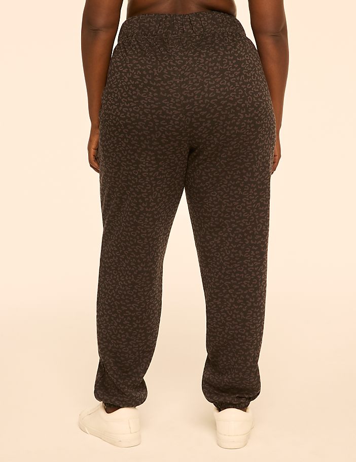 A person wearing patterned sweatpants and white sneakers stands against a plain, light-colored background.