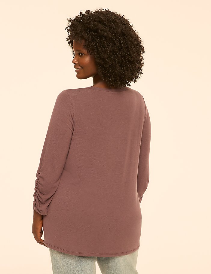 A woman with curly dark hair, wearing a mauve long-sleeved shirt, is shown from the back against a plain, light peach background.