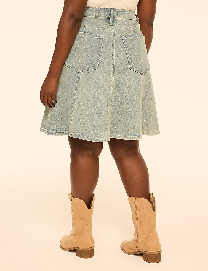 A person wearing a light-wash denim skirt and tan cowboy boots stands against a plain, light-colored background.