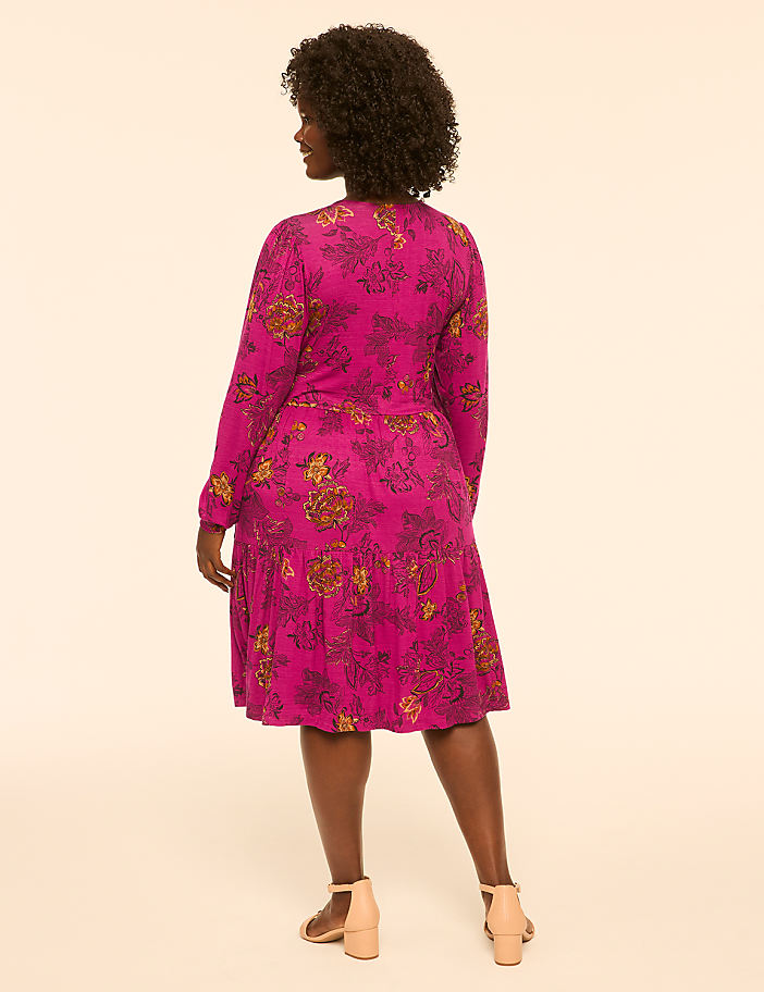 A woman in a floral pink dress stands against a plain, light-colored background.