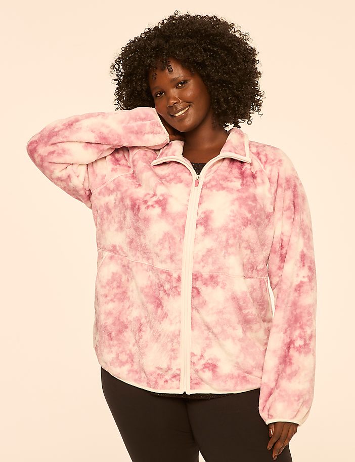 A smiling woman with dark curly hair poses in a pink tie-dye jacket against a plain, light-colored background.